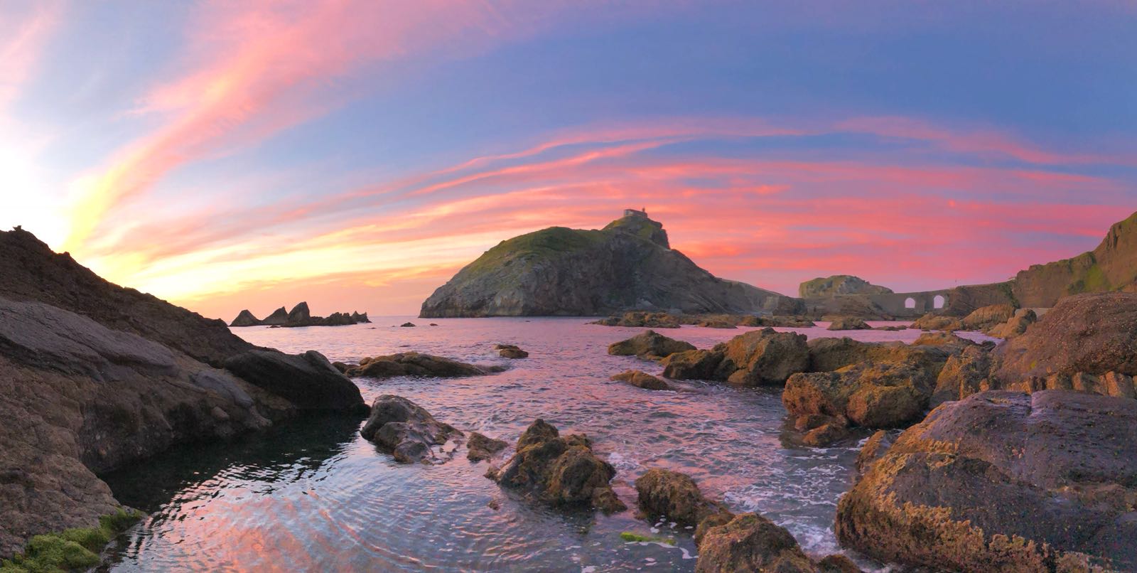 Costa rocosa con un puente y cielo rosa al atardecer